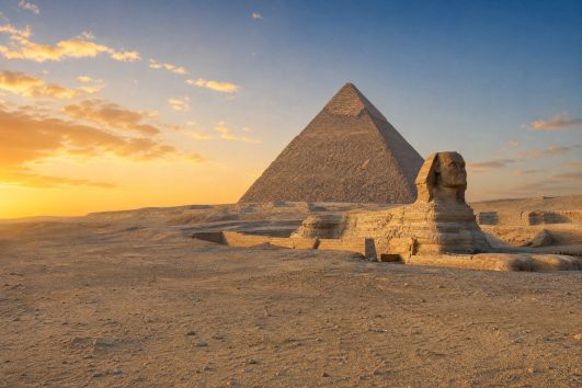 Great Pyramid and Sphinx on the Giza Plateau in warm dawn light.