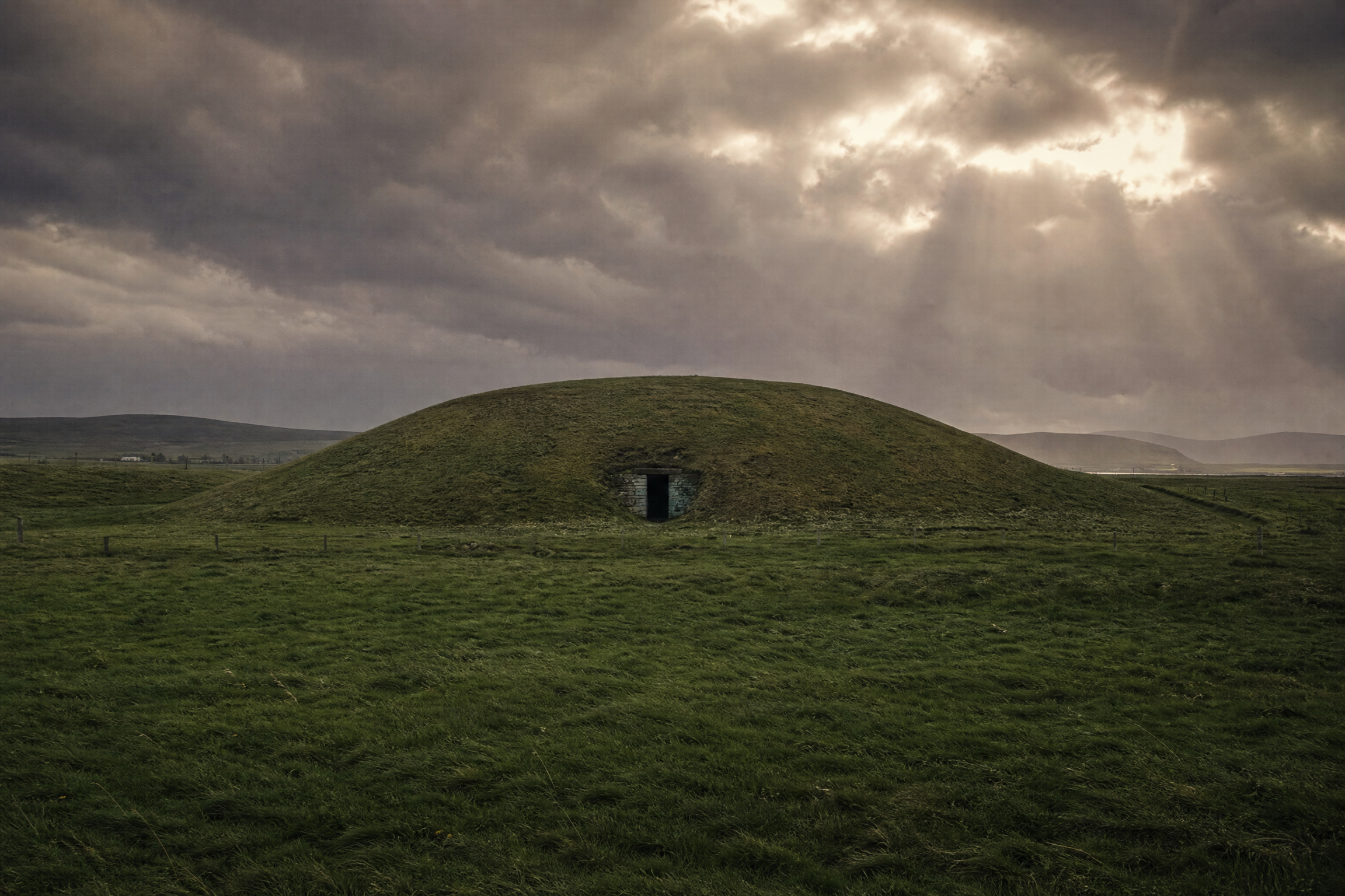 Exterior mound of the Maeshowe chambered cairn, Orkney, under a dramatic stormy sky