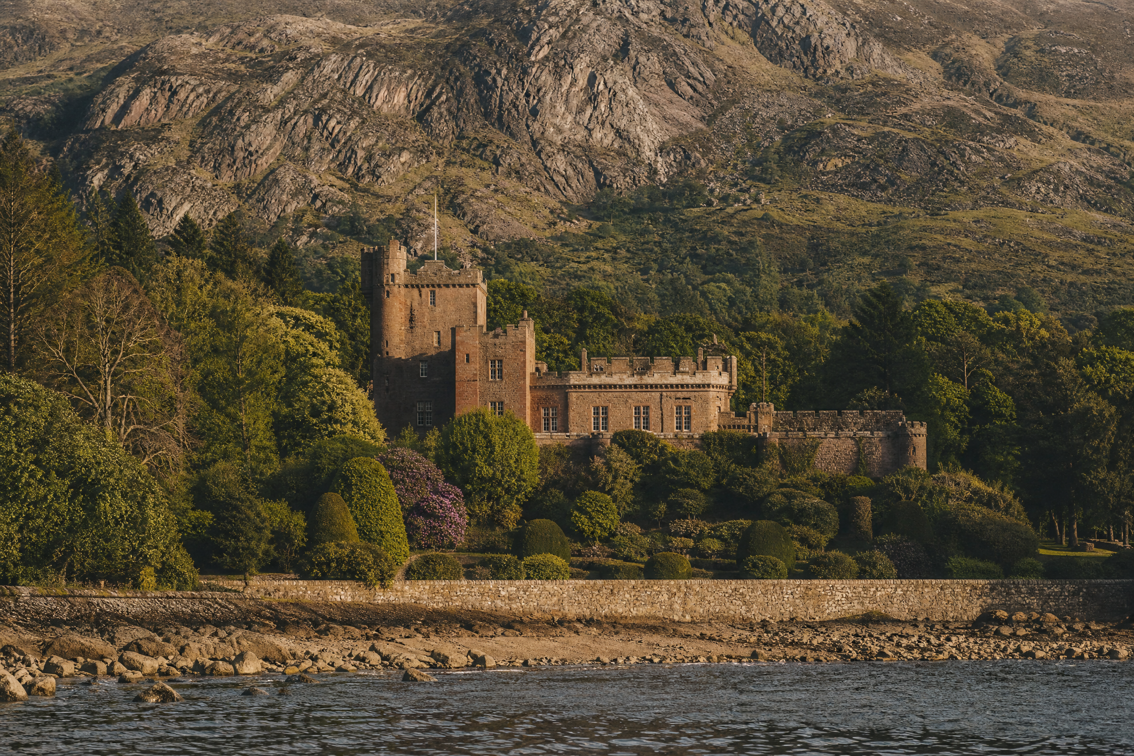 Brodick Castle, a red sandstone castle on the Isle of Arran, viewed from the bay against granite mountains, Scotland