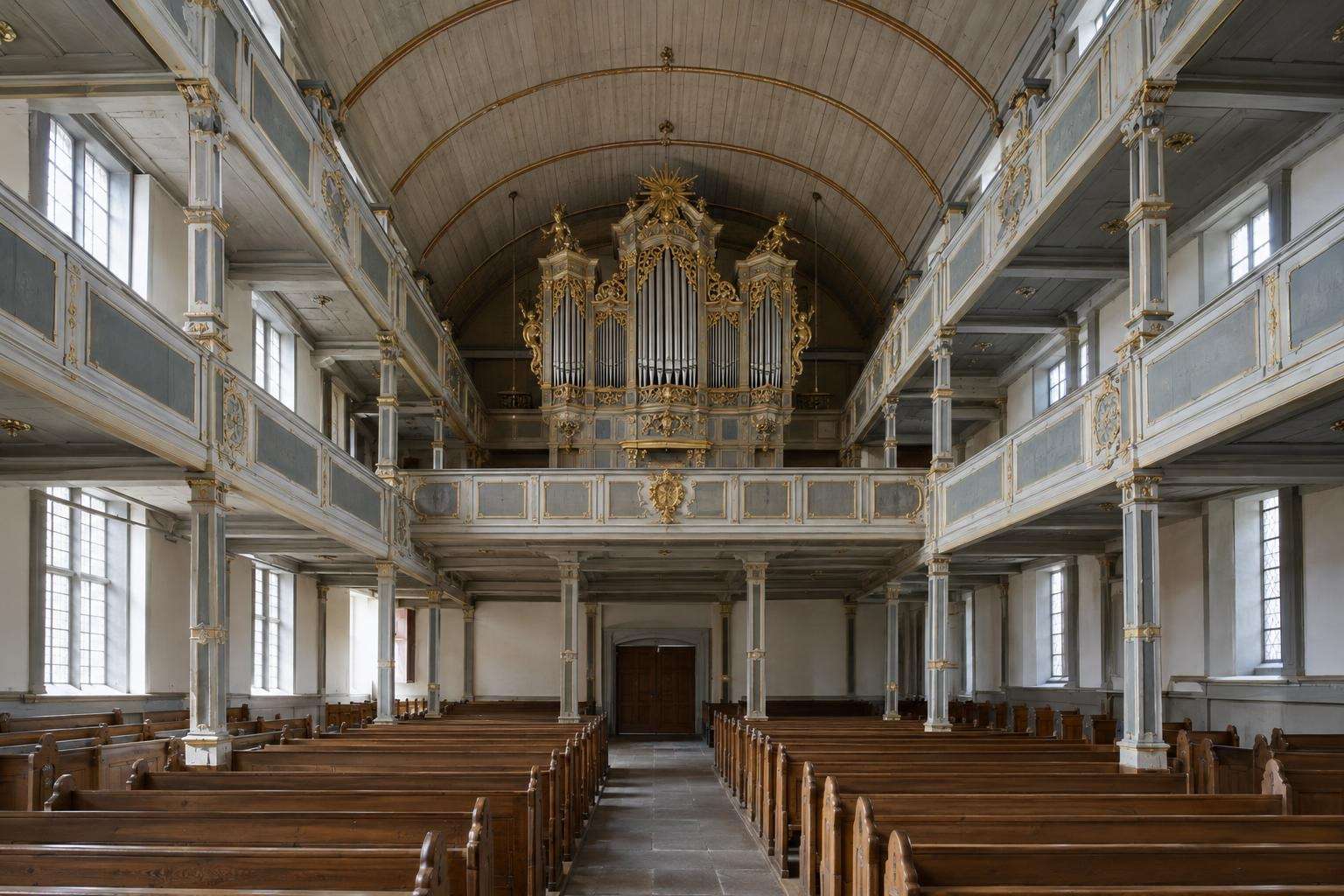 A Baroque hall church interior with three tiers of wooden galleries, a wooden barrel-vaulted ceiling and an organ on the top gallery in Arnstadt, Thuringia