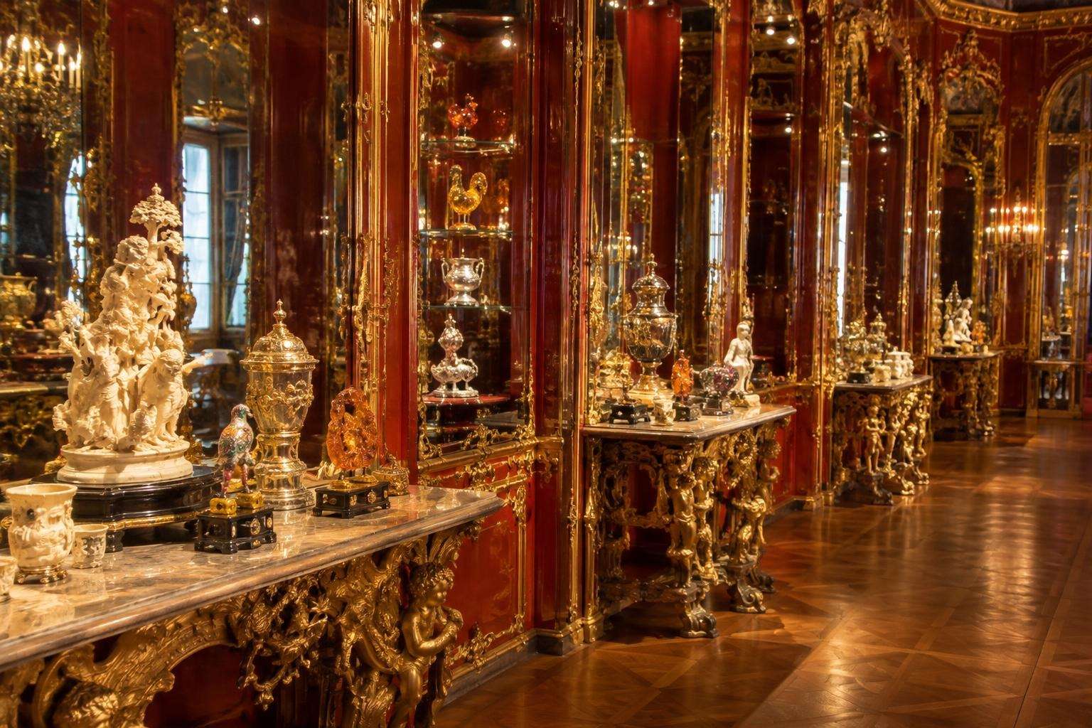 A Baroque treasury room with mirrored walls and gilded shelves displaying precious objects of gold, silver and jewels in Dresden, Germany