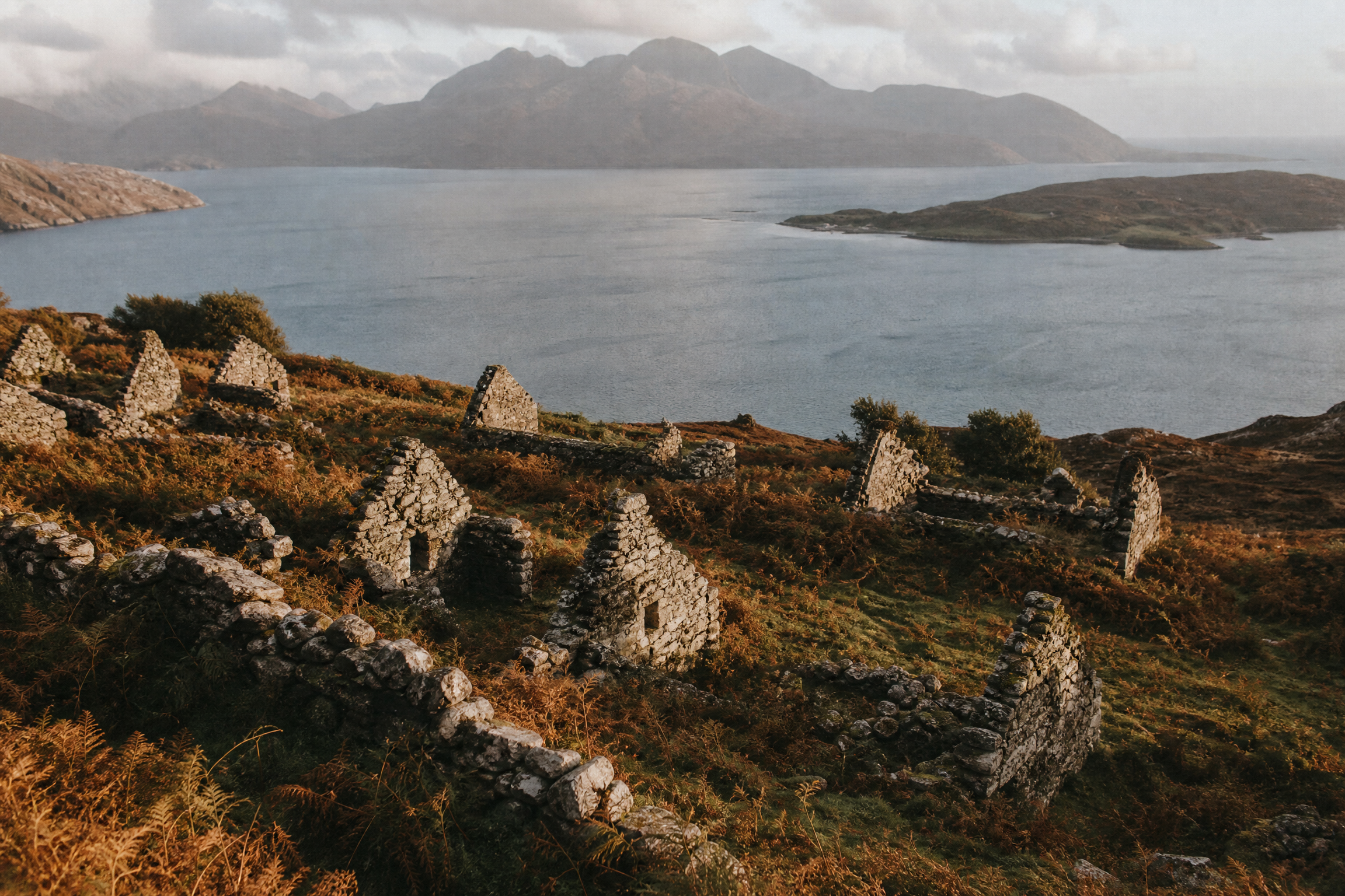 Roofless stone cottages of a deserted crofting township above a sea loch on Skye