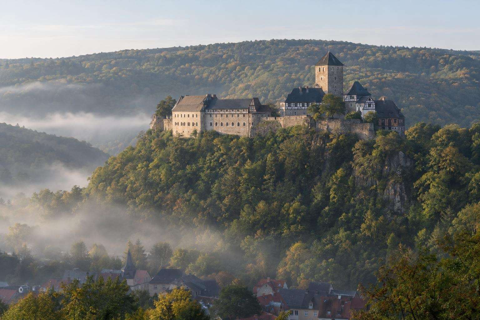 A medieval castle on a forested ridge above the town of Eisenach in Thuringia, Germany, in soft morning light