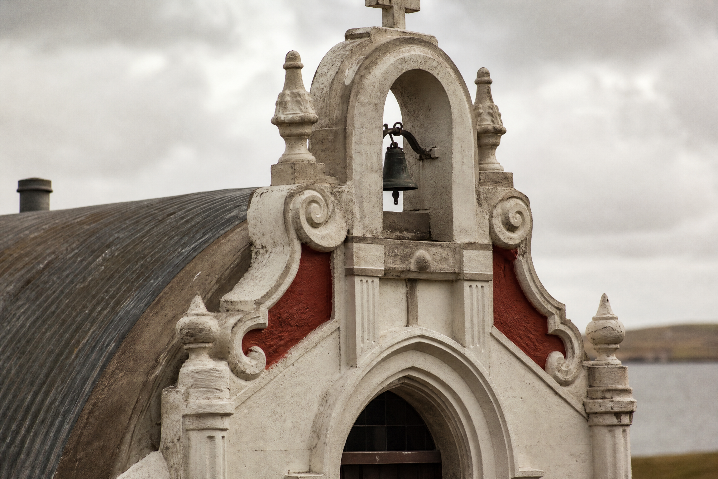 Close-up of the Italian Chapel's facade detail, showing the bell turret, baroque scroll pinnacles and red-and-white cement decoration