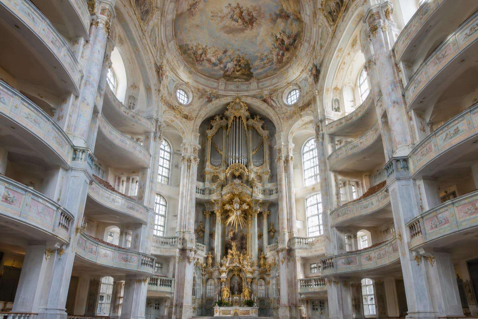 The interior of a domed Baroque church with tiers of curved galleries in white, gold and pastel colours rising to a painted dome in Dresden