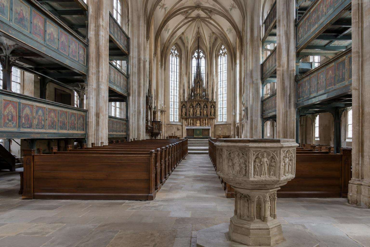The interior of a late-Gothic three-aisled hall church with tiered wooden galleries and a carved stone baptismal font in Eisenach, Thuringia