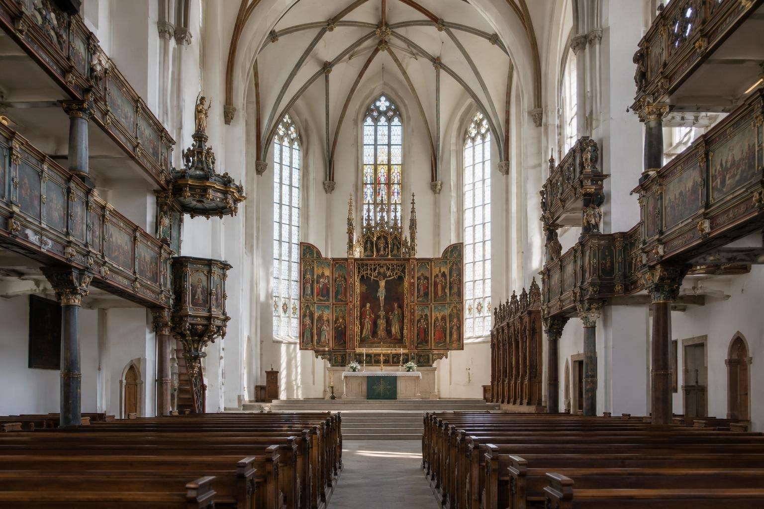 The interior of a Gothic town church in Weimar with a painted Renaissance winged altarpiece, white walls and wooden pews