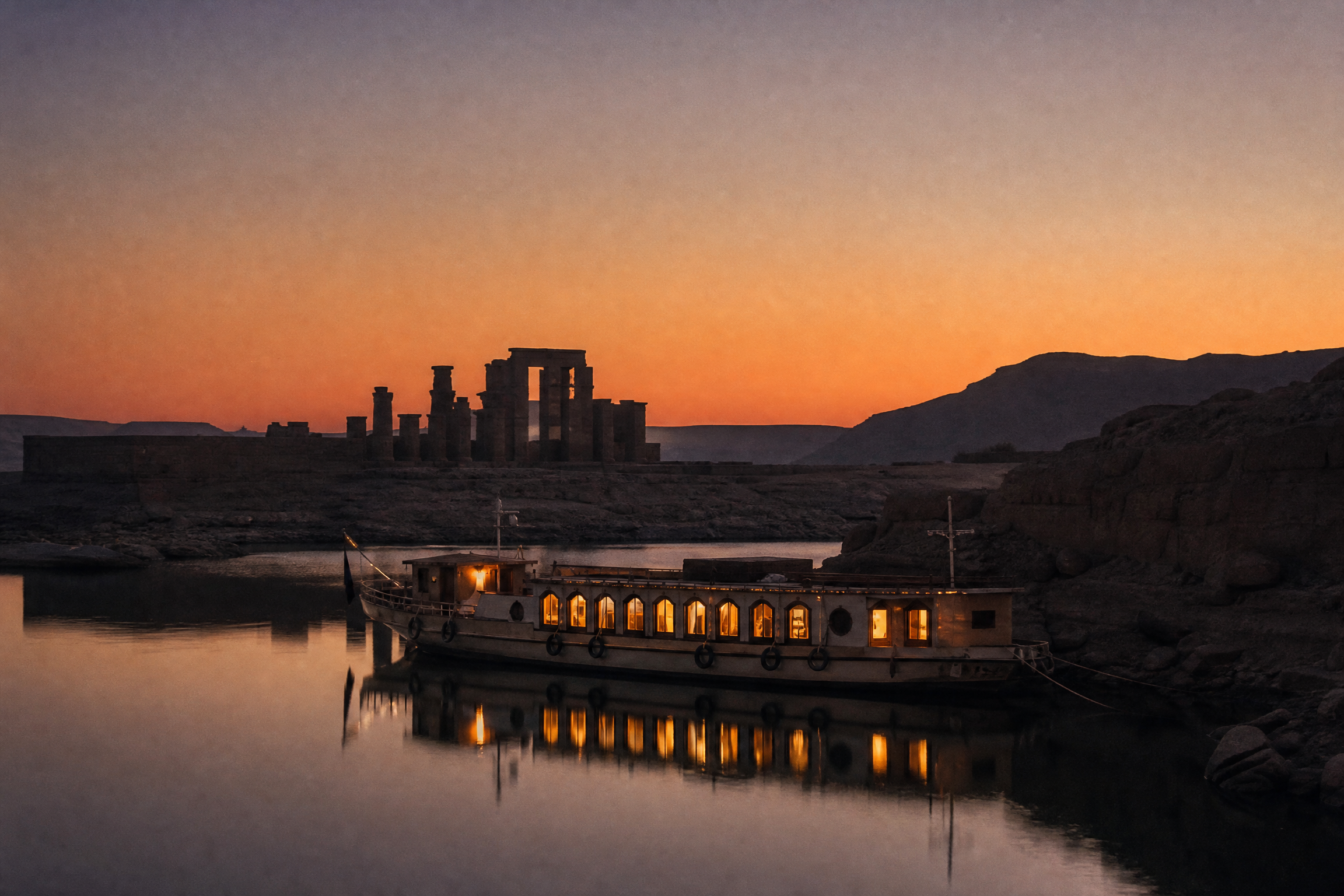Small cruise vessel moored on the still waters of Lake Nasser at dusk, beside a Nubian temple