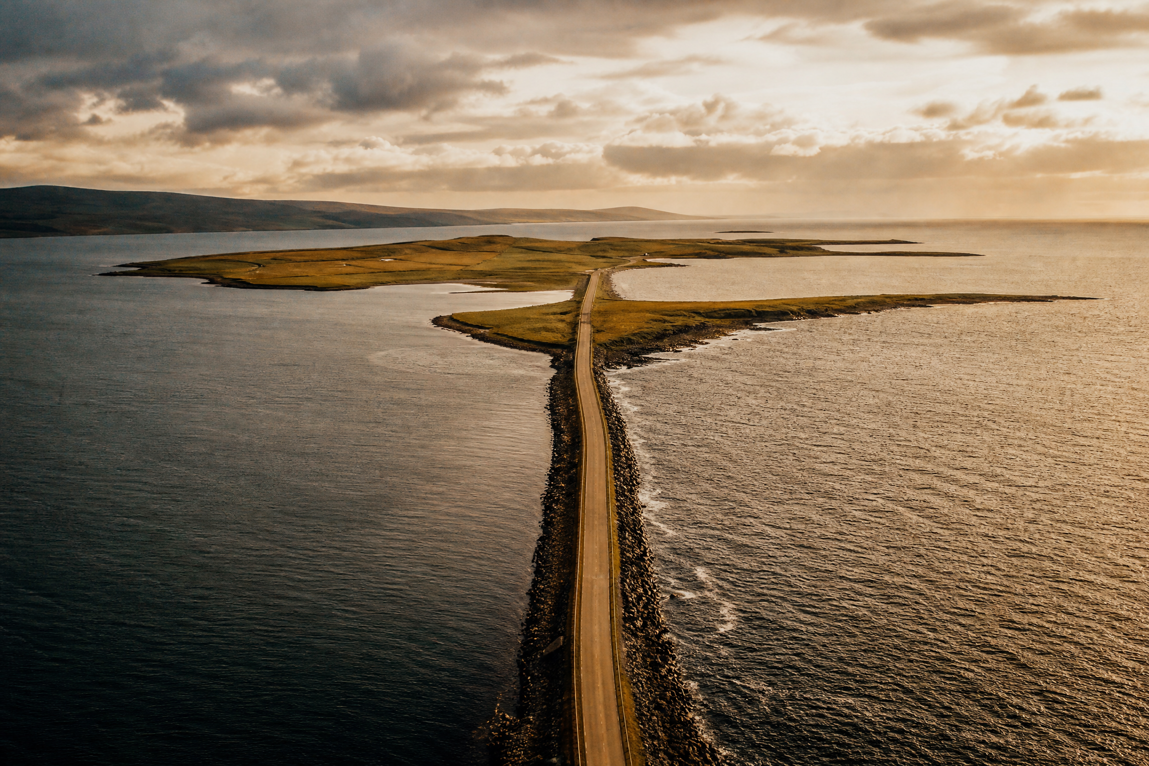 Aerial view of a single Churchill Barrier causeway crossing a tidal channel in Orkney, Scotland, in golden light