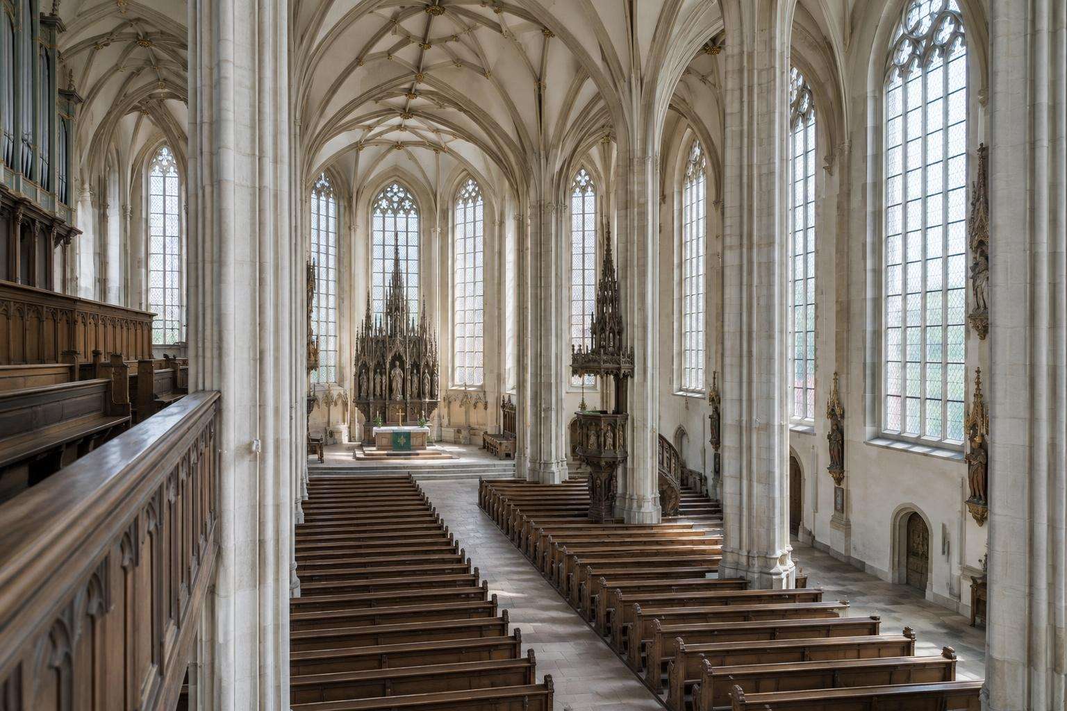 The nave of a late-Gothic Lutheran hall church in Leipzig, Saxony, with tall windows, pale stone piers and wooden pews