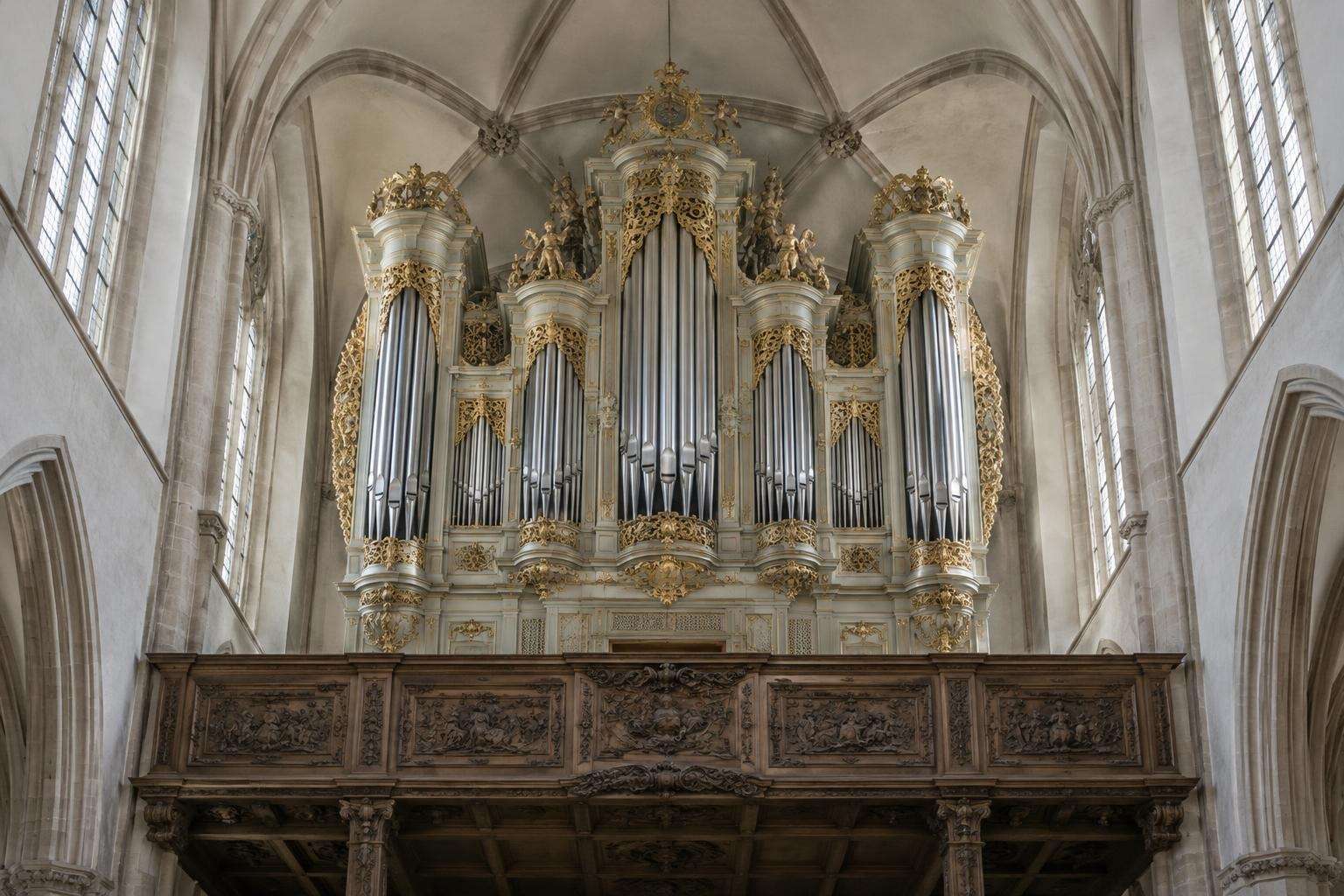 A carved wooden organ case with silver pipes in the west gallery of a late-Gothic church in Leipzig, seen from the nave