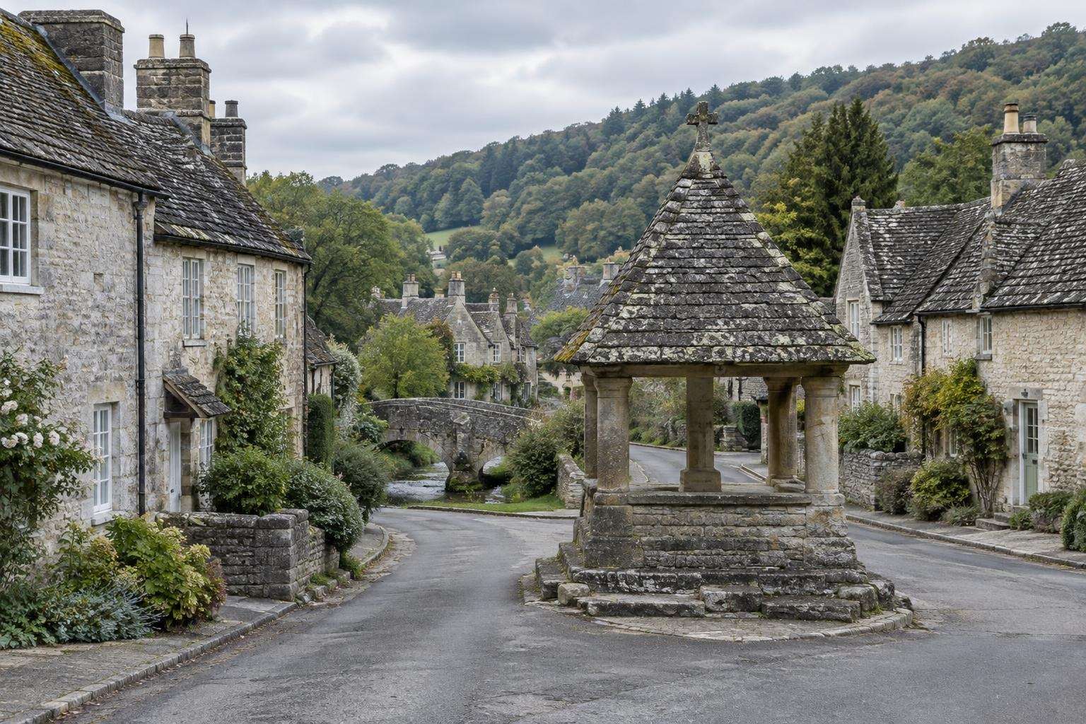Pale grey limestone cottages and a stone-roofed market cross in a village in the southern Cotswolds.
