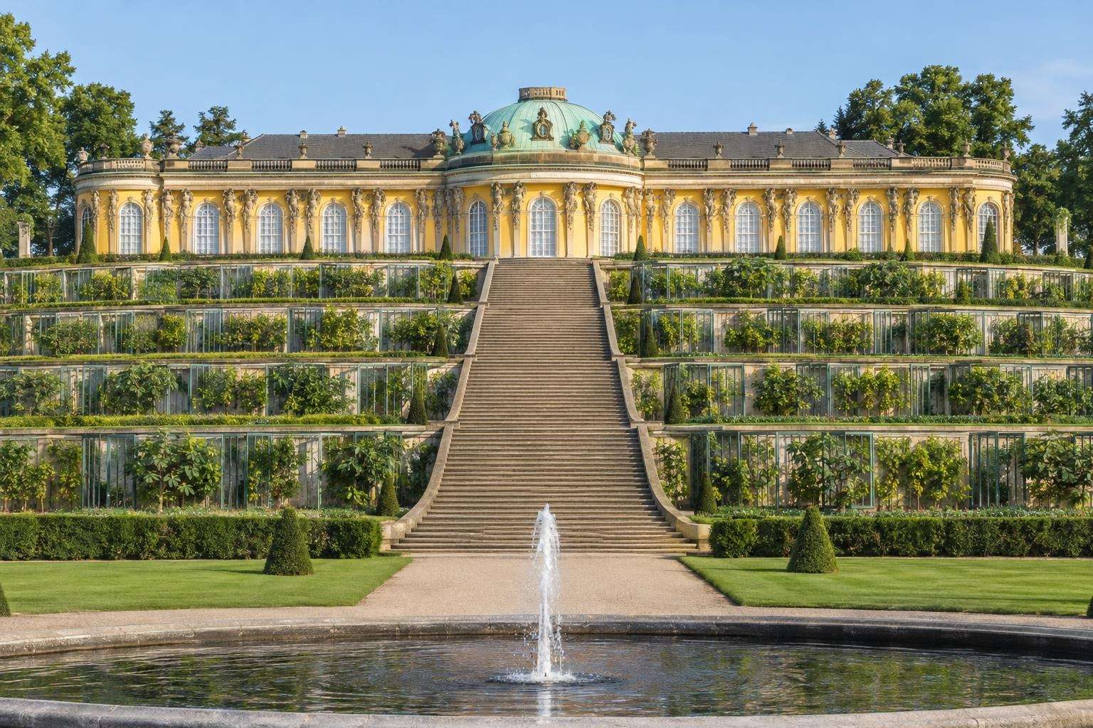 A single-storey yellow rococo palace with a green dome above terraced vineyards and glass-fronted niches in Potsdam, Germany