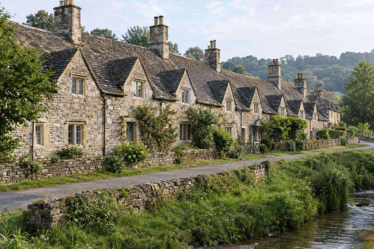 A terrace of limestone weavers' cottages with steep stone-slate roofs and gables in a Cotswold village.