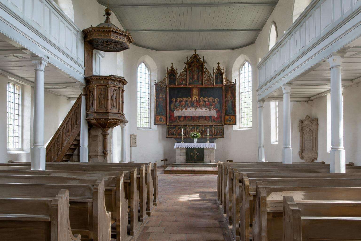 The interior of a small Baroque Lutheran church with white wooden galleries, a carved pulpit and a sixteenth-century painted altarpiece in Köthen, Germany