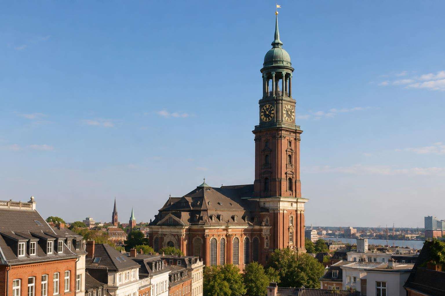 A tall Baroque church tower of red brick with a green copper cupola and clock rising above the rooftops of Hamburg on a clear day