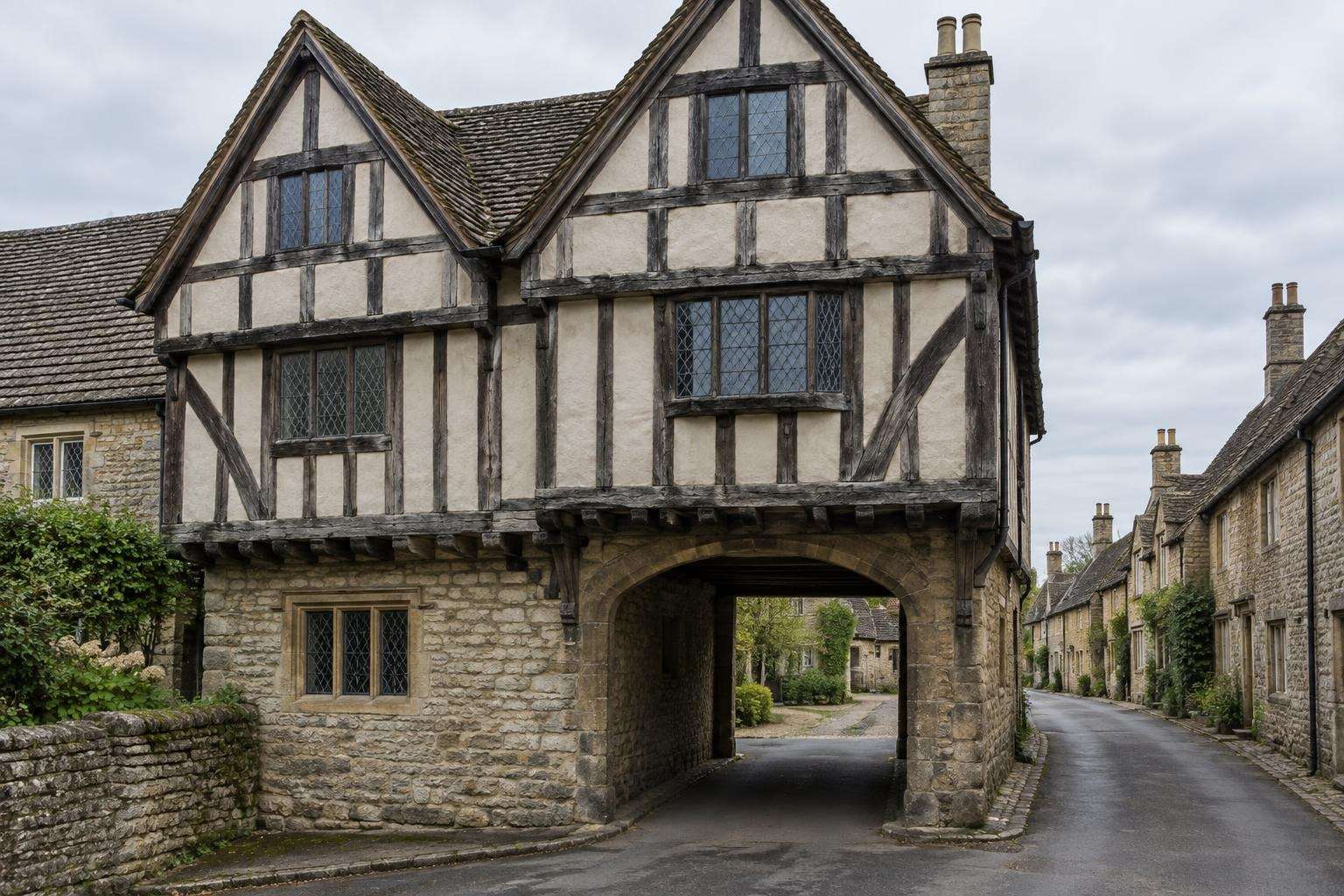 A late-medieval timber-framed building with jettied gables and an entrance passage on a street in Lacock, Wiltshire.